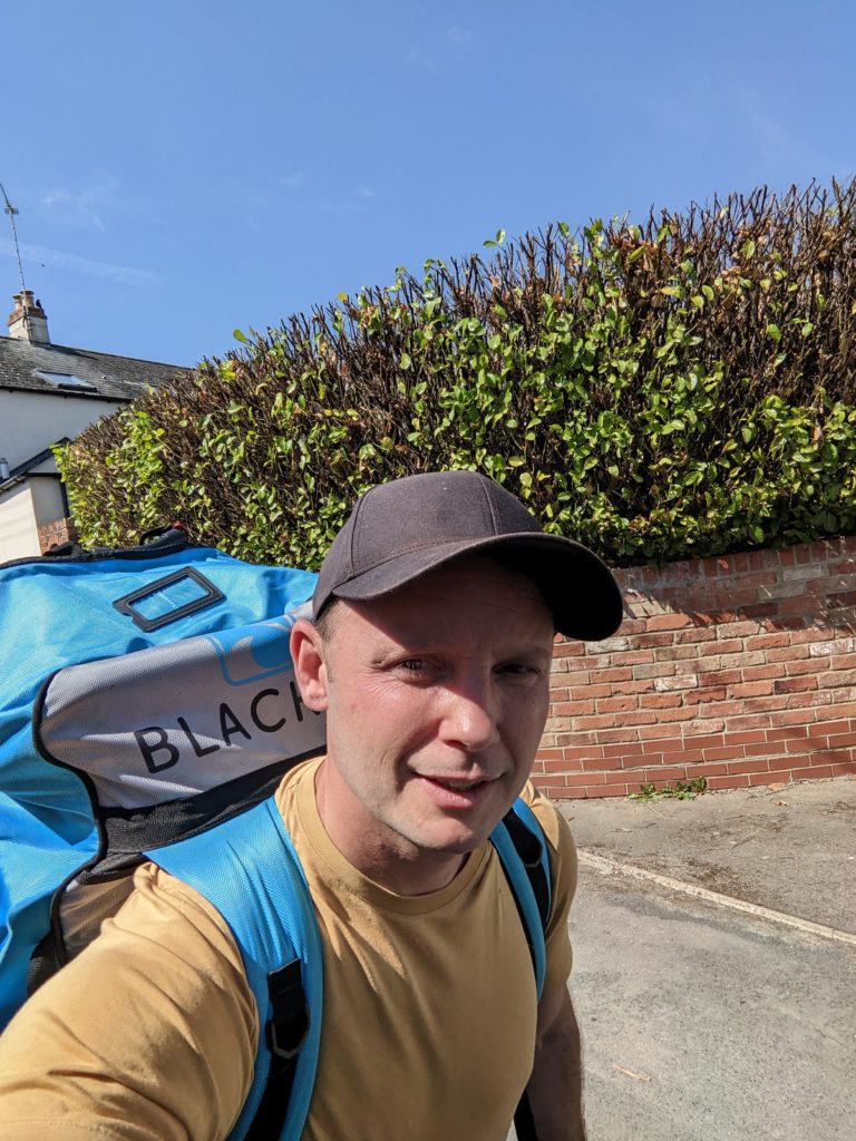 Tom carrying paddleboard on back in bag, on the way to paddle board the thames