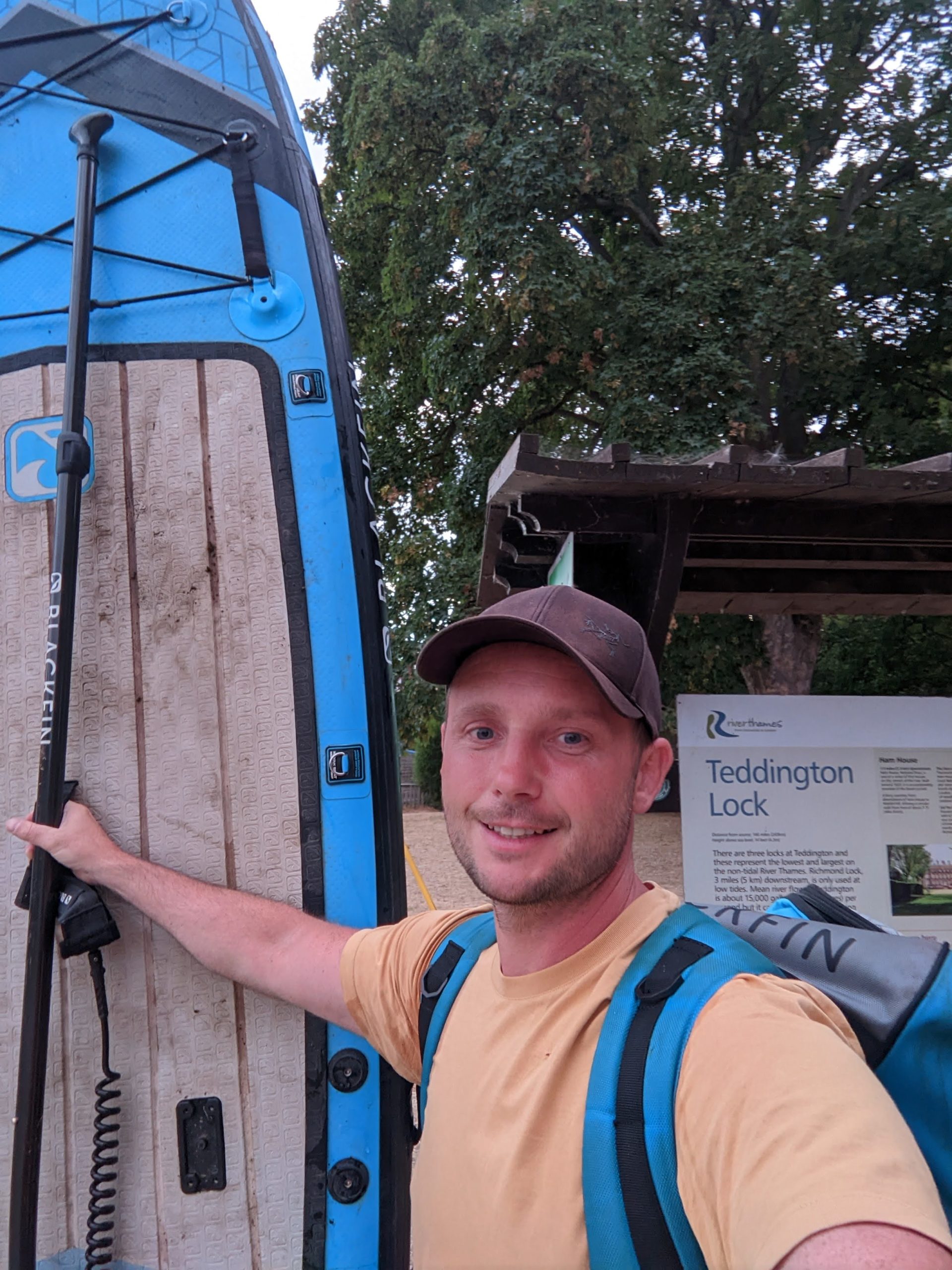 Tom standing with paddle board at Teddington Lock sign after paddle boarding the thames